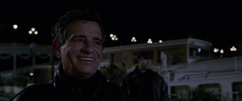 Movie still from “Ronin” (1998), directed by John Frankenheimer – A person smiling at night; Close Up shot, Low angle