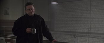 Movie still from “Ronin” (1998), directed by John Frankenheimer – A man standing in a dark room holding a cup; Medium shot, Low angle