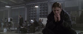 Movie still from “Ronin” (1998), directed by John Frankenheimer – A man sitting in front of a group of speakers; Medium shot, Low angle