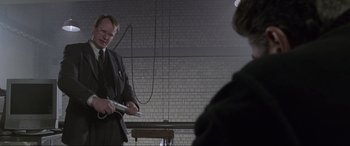 Movie still from “Ronin” (1998), directed by John Frankenheimer – A man in a suit and tie holding a cell phone in his hands; Medium shot, Low angle