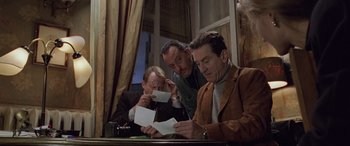 Movie still from “Ronin” (1998), directed by John Frankenheimer – A group of people sitting at a table looking at papers; Medium shot, Over the shoulder angle