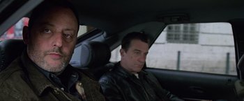 Movie still from “Ronin” (1998), directed by John Frankenheimer – A man sitting in the back seat of a car next to another man; Close Up shot, Over the shoulder angle