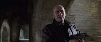 Movie still from “Ronin” (1998), directed by John Frankenheimer – A bald man wearing a leather jacket in front of a brick wall; Close Up shot, Low angle