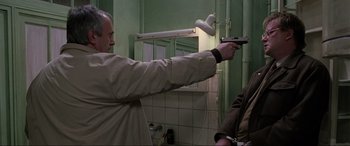 Movie still from “Ronin” (1998), directed by John Frankenheimer – A man holding a gun pointed at a mirror; Medium shot, Over the shoulder angle