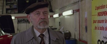 Movie still from “Ronin” (1998), directed by John Frankenheimer – An older man wearing a hat and a tie; Close Up shot, Low angle