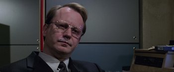 Movie still from “Ronin” (1998), directed by John Frankenheimer – A person wearing a suit and glasses; Close Up shot, Low angle