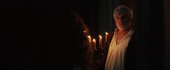 Movie still from “Rosaline” (2022), directed by Karen Maine – An older woman standing in front of a group of lit candles; Medium shot, Over the shoulder angle