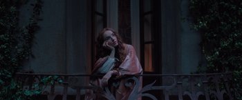 Movie still from “Rosaline” (2022), directed by Karen Maine – A woman leaning on a railing in front of a window; Medium shot, Low angle
