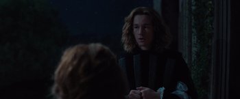 Movie still from “Rosaline” (2022), directed by Karen Maine – A man with long brown hair is talking to a woman; Medium shot, Over the shoulder angle