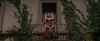 Movie still from “Rosaline” (2022), directed by Karen Maine – A woman dressed in medieval clothing standing on a balcony railing; Wide shot, Low angle