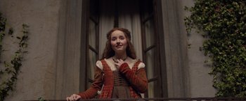 Movie still from “Rosaline” (2022), directed by Karen Maine – A young woman in medieval clothing standing in front of a window; Medium shot, Low angle
