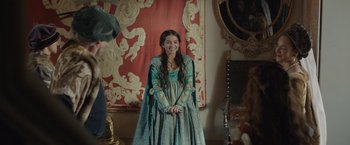 Movie still from “Rosaline” (2022), directed by Karen Maine – A woman in a medieval dress smiling for the camera; Medium shot, Over the shoulder angle