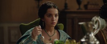 Movie still from “Rosaline” (2022), directed by Karen Maine – A woman sitting at a dinner table holding a spoon; Close Up shot, Over the shoulder angle