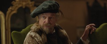 Movie still from “Rosaline” (2022), directed by Karen Maine – An old man with a beard wearing a hat; Close Up shot, Over the shoulder angle