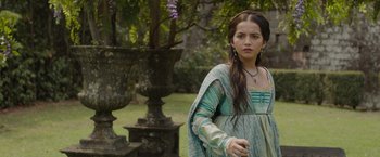 Movie still from “Rosaline” (2022), directed by Karen Maine – A woman in a medieval dress standing in front of a tree; Medium shot, Over the shoulder angle