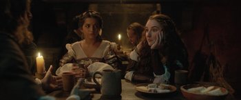Movie still from “Rosaline” (2022), directed by Karen Maine – A group of people sitting at a table with a candle; Medium shot, Over the shoulder angle
