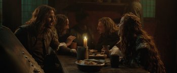Movie still from “Rosaline” (2022), directed by Karen Maine – A group of people sitting around a table with a candle; Medium shot, Over the shoulder angle