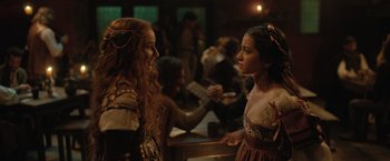 Movie still from “Rosaline” (2022), directed by Karen Maine – Two women in medieval garb talking to each other in a bar; Medium shot, Over the shoulder angle