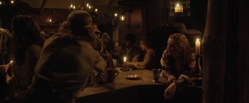 Movie still from “Rosaline” (2022), directed by Karen Maine – A group of people sitting at a table with candles; Medium shot, Over the shoulder angle