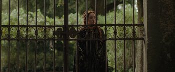 Movie still from “Rosaline” (2022), directed by Karen Maine – A woman standing in front of an iron gate; Medium shot, Over the shoulder angle