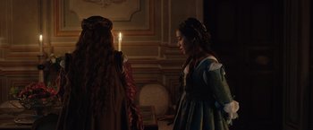 Movie still from “Rosaline” (2022), directed by Karen Maine – Two women dressed in medieval clothing standing in front of a lit candle; Medium shot, Over the shoulder angle