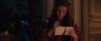 Movie still from “Rosaline” (2022), directed by Karen Maine – A young woman opening a gift box in front of a window; Close Up shot, Over the shoulder angle
