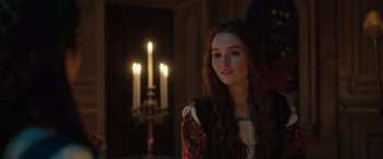 Movie still from “Rosaline” (2022), directed by Karen Maine – A young woman in medieval garb standing in front of candles; Close Up shot, Over the shoulder angle