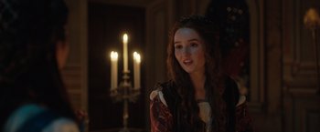 Movie still from “Rosaline” (2022), directed by Karen Maine – A young woman in a medieval dress in front of candles; Close Up shot, Over the shoulder angle