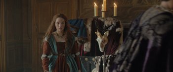 Movie still from “Rosaline” (2022), directed by Karen Maine – A woman standing in front of a mirror with candles on the wall; Medium shot, Over the shoulder angle