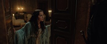 Movie still from “Rosaline” (2022), directed by Karen Maine – A woman standing in front of a wooden door; Medium shot, Over the shoulder angle
