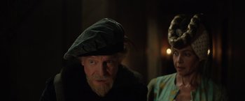 Movie still from “Rosaline” (2022), directed by Karen Maine – An old man wearing a hat and a beard; Medium shot, Over the shoulder angle