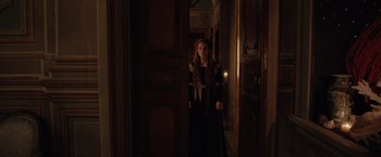 Movie still from “Rosaline” (2022), directed by Karen Maine – A woman standing in a dark room with a candle in her hand; Medium shot, Over the shoulder angle