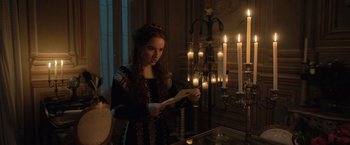 Movie still from “Rosaline” (2022), directed by Karen Maine – A woman in a black dress standing in front of candles; Medium shot, Over the shoulder angle