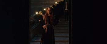 Movie still from “Rosaline” (2022), directed by Karen Maine – A woman standing on some steps wearing a black dress; Medium shot, Over the shoulder angle