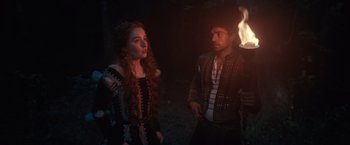 Movie still from “Rosaline” (2022), directed by Karen Maine – A man and a woman standing next to each other in front of a fire; Medium shot, Over the shoulder angle