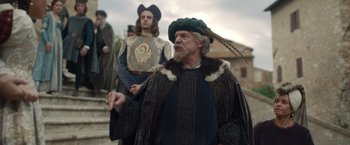 Movie still from “Rosaline” (2022), directed by Karen Maine – A man with a long beard wearing a hat and holding a feather; Medium shot, Over the shoulder angle