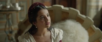 Movie still from “Rosaline” (2022), directed by Karen Maine – A young woman in a red hat and white dress; Close Up shot, Over the shoulder angle