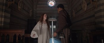 Movie still from “Rosaline” (2022), directed by Karen Maine – A man and a woman are standing in front of a stained glass window; Medium shot, Low angle