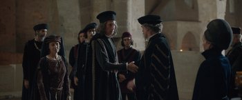 Movie still from “Rosaline” (2022), directed by Karen Maine – Two men in medieval garb shaking hands in a building; Medium shot, Over the shoulder angle