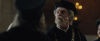 Movie still from “Rosaline” (2022), directed by Karen Maine – An old man with a beard wearing a black hat; Close Up shot, Over the shoulder angle