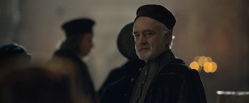 Movie still from “Rosaline” (2022), directed by Karen Maine – An older man with a beard wearing a black hat; Close Up shot, Over the shoulder angle