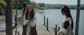 Movie still from “Rosaline” (2022), directed by Karen Maine – A woman in medieval garb standing next to a body of water; Medium shot, Over the shoulder angle