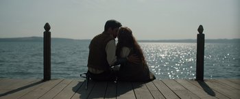 Movie still from “Rosaline” (2022), directed by Karen Maine – A man and a woman sitting on a dock by the water; Medium shot, Over the shoulder angle