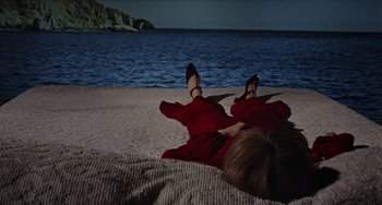 Movie still from “Rosemary's Baby” (1968), directed by Roman Polanski – A woman laying on the beach in a red dress; Wide shot, High angle