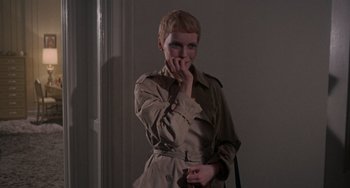 Movie still from “Rosemary's Baby” (1968), directed by Roman Polanski – A woman wearing a trench coat is holding her hand to her mouth; Medium shot, Over the shoulder angle