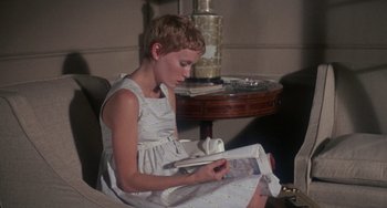 Movie still from “Rosemary's Baby” (1968), directed by Roman Polanski – A young girl sitting on a chair reading a book; Medium shot, High angle