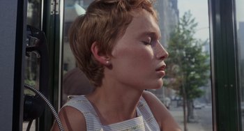 Movie still from “Rosemary's Baby” (1968), directed by Roman Polanski – A woman with short brown hair sitting in front of a building; Close Up shot, High angle
