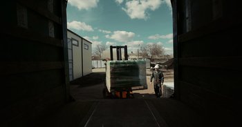 Movie still from “Rucker” (2022), directed by Amy Hesketh – A man standing in front of a truck with boxes on it; Extreme Wide shot, High angle