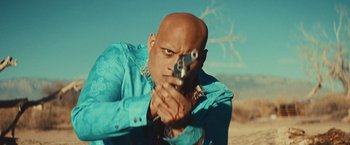 Movie still from “Run & Gun” (2022), directed by Christopher Borrelli – A bald man in a blue shirt is holding a gun; Close Up shot, Low angle