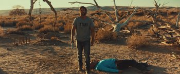 Movie still from “Run & Gun” (2022), directed by Christopher Borrelli – A man standing next to a dead body in the desert; Wide shot, Over the shoulder angle